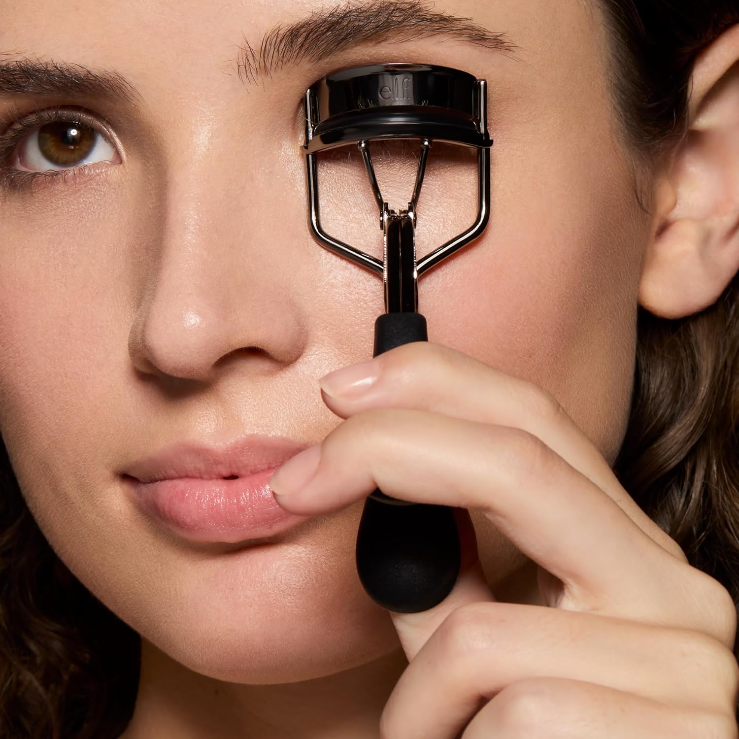 Model holding the e.l.f. Pro Eyelash Curler against her lash line, showing how wide the head sits over the eye