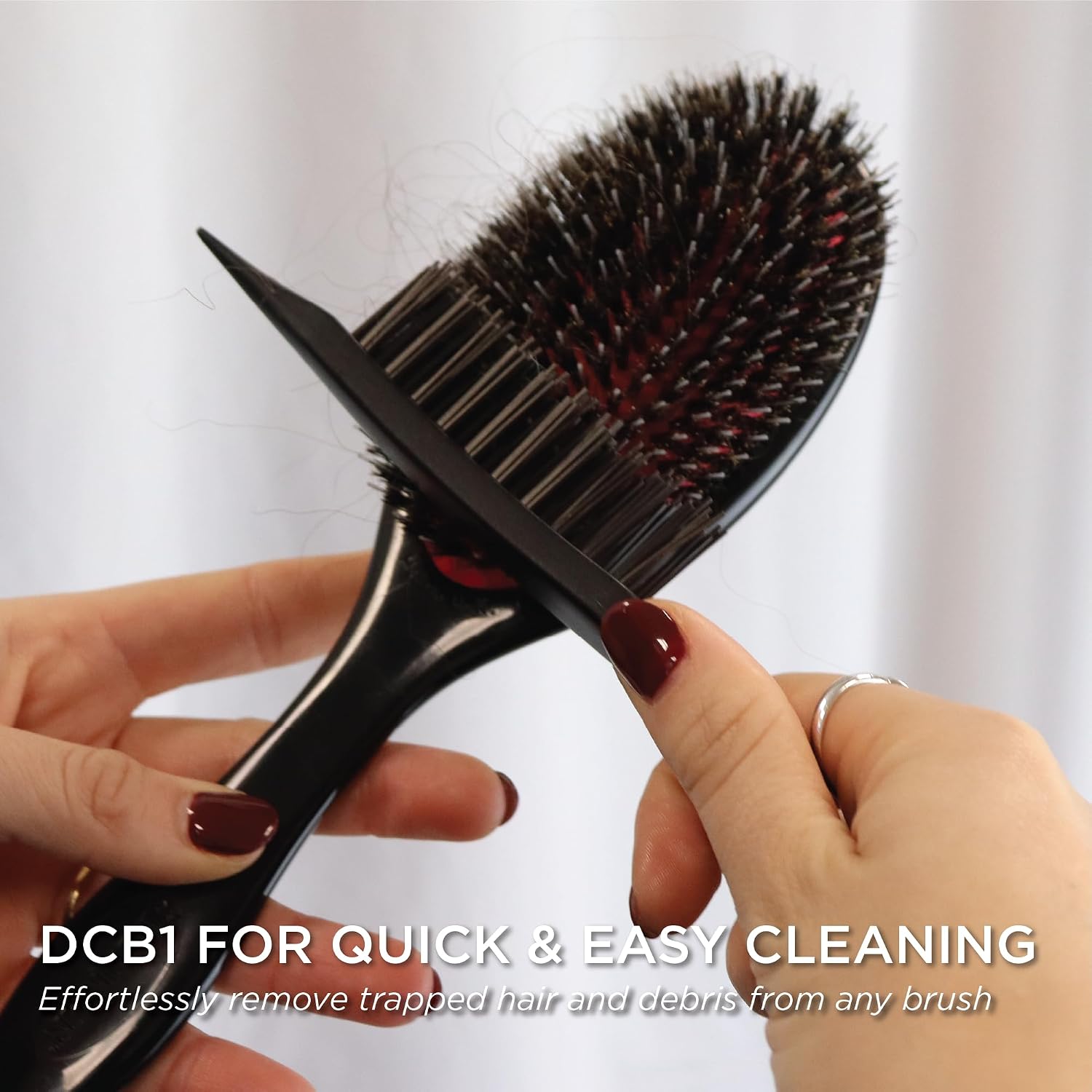 The Denman DCB1 pointed tip being drawn through the bristles of a dark hairbrush to lift out trapped hair