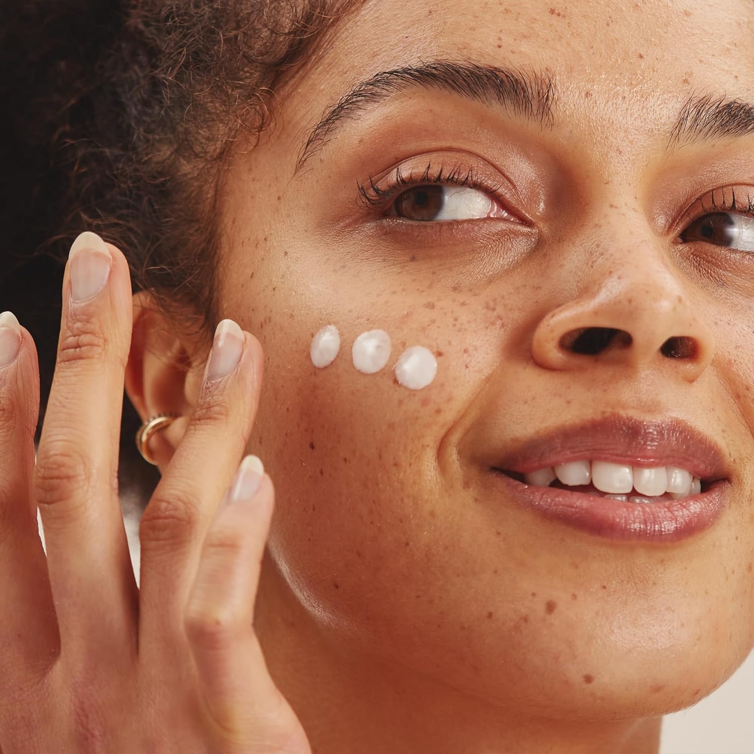 Model applying three small dots of Dermatica azelaic acid cream to her cheek with her fingertips