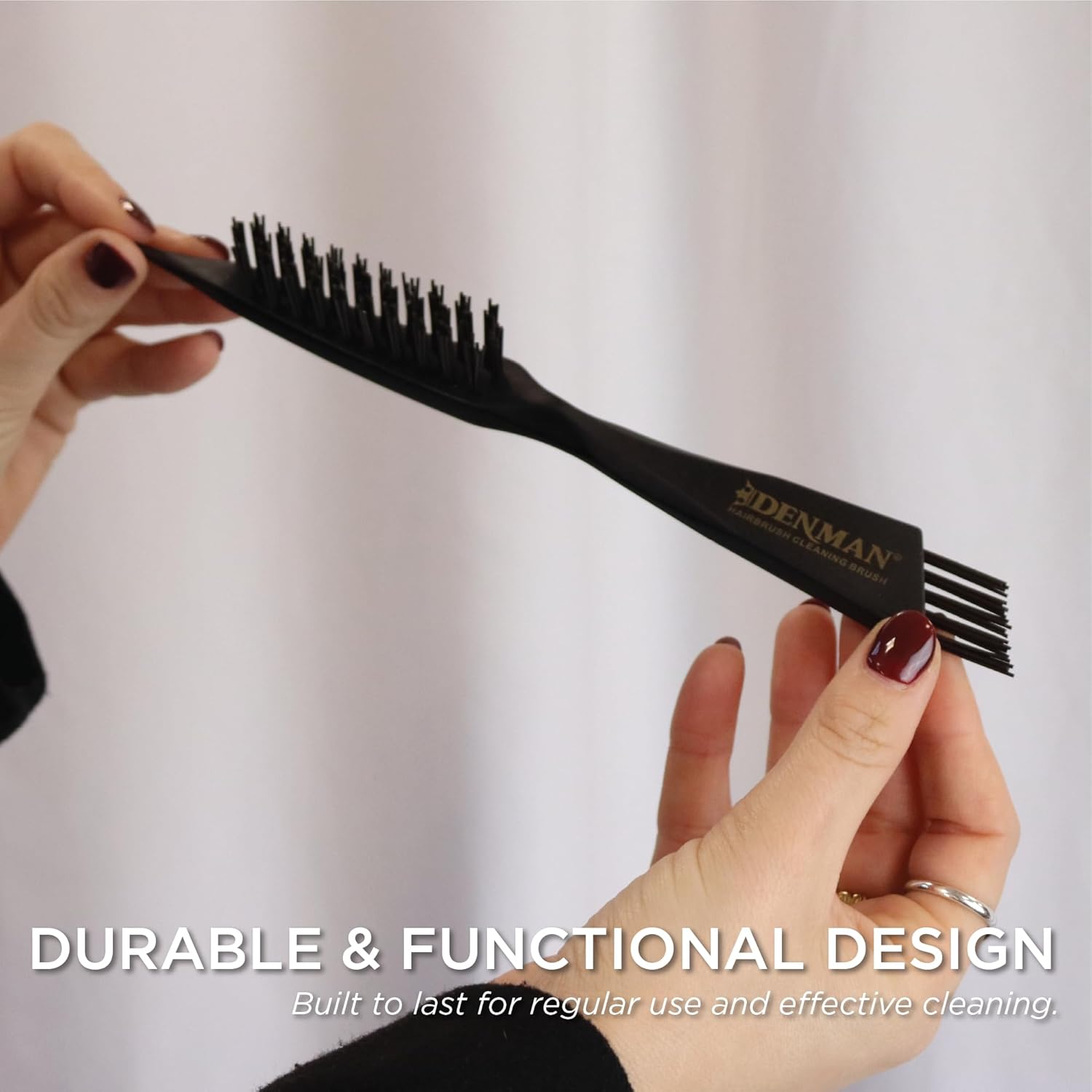 Hand holding the Denman DCB1 cleaning brush, showing the row of long thin prongs at the base of the handle