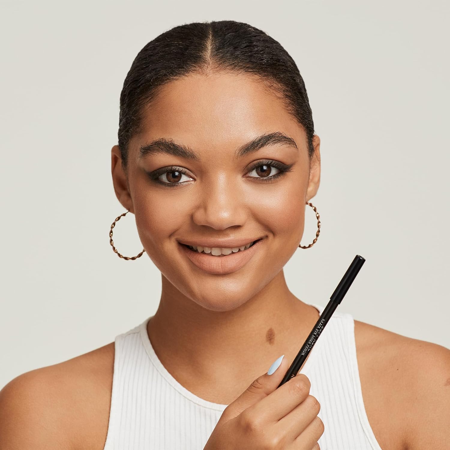 Smiling model with eyeliner applied holding the Rimmel Soft Kohl pencil