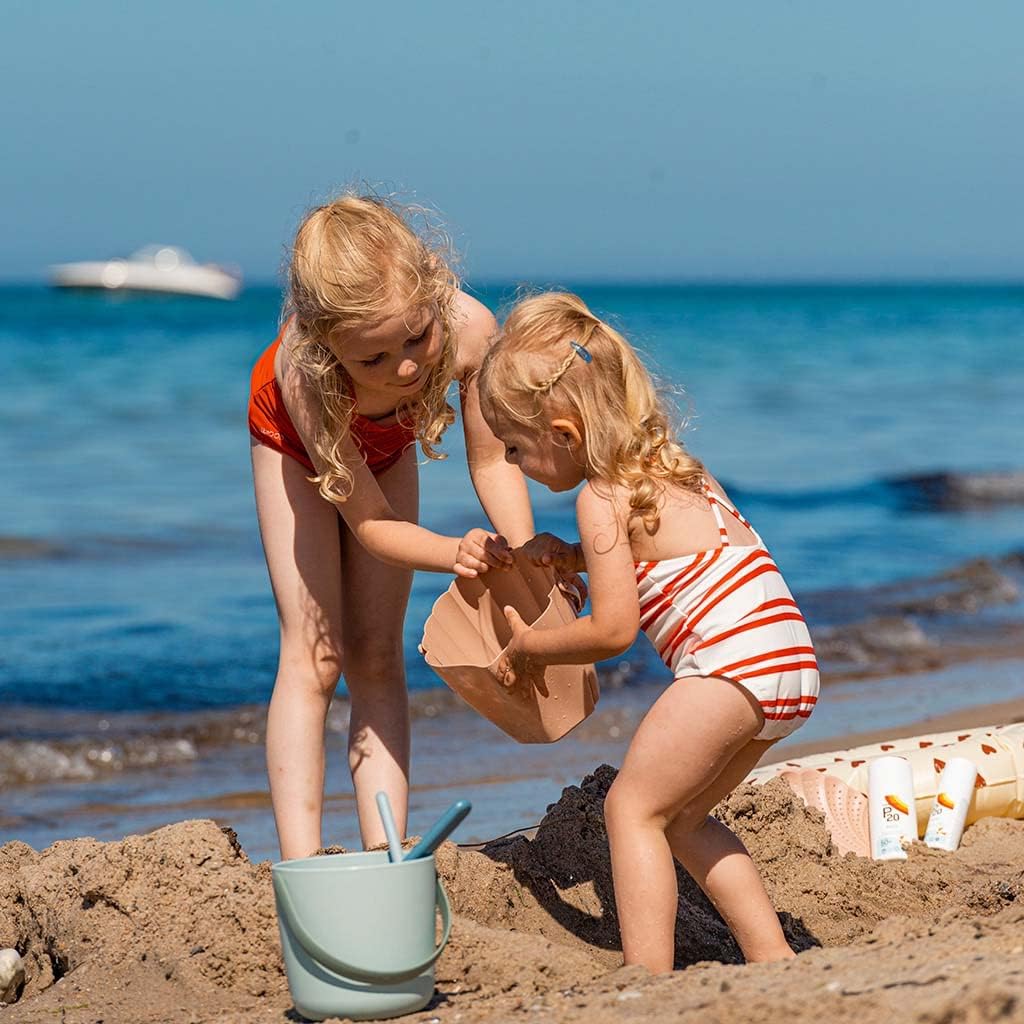 Two young children playing on a sunny beach with P20 Kids bottles on a mat behind them