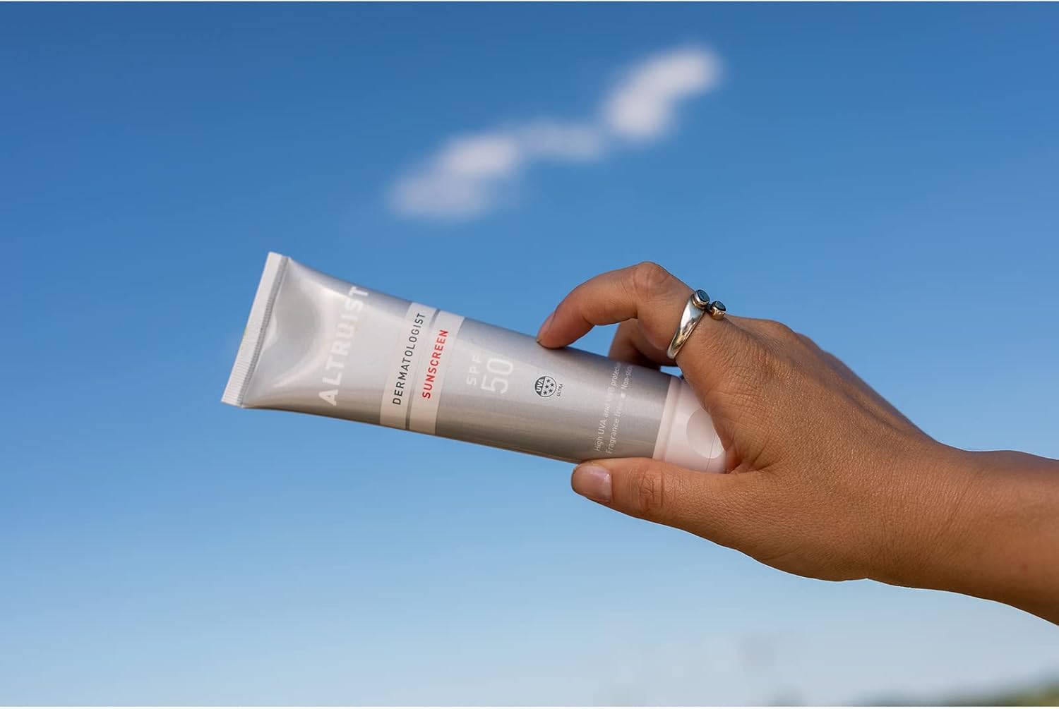 Woman applying SPF 50 sunscreen to her face outdoors on a bright day