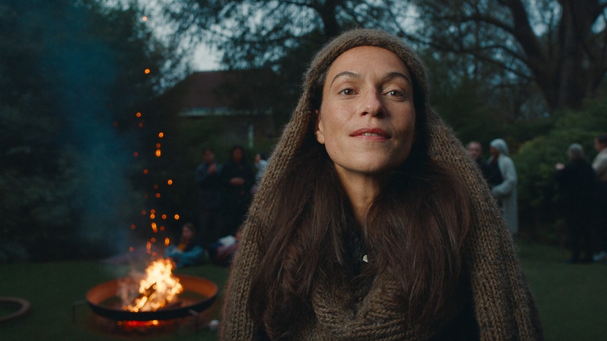Woman with long hair tucked under a knitted hood and scarf standing in a UK garden beside a bonfire on a smoky November evening
