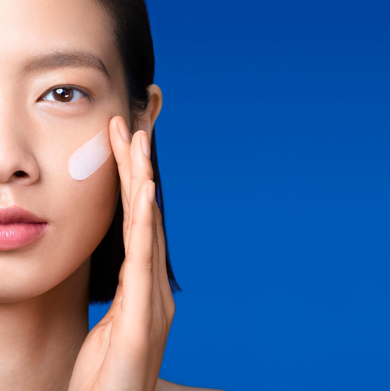 Model with La Roche-Posay Anthelios sunscreen drop on cheek against blue background