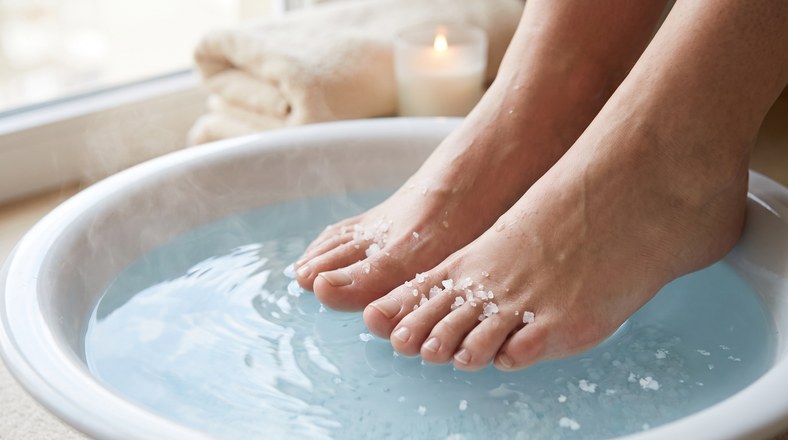 Bare feet soaking in a warm Epsom salt bath to soften dry, rough skin