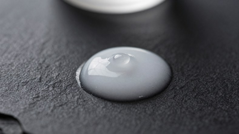 Near-invisible droplet of hybrid nano mineral sunscreen on black stone showing minimal white cast