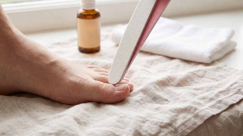 Emery board shaping a toenail during an at-home pedicure for dry feet
