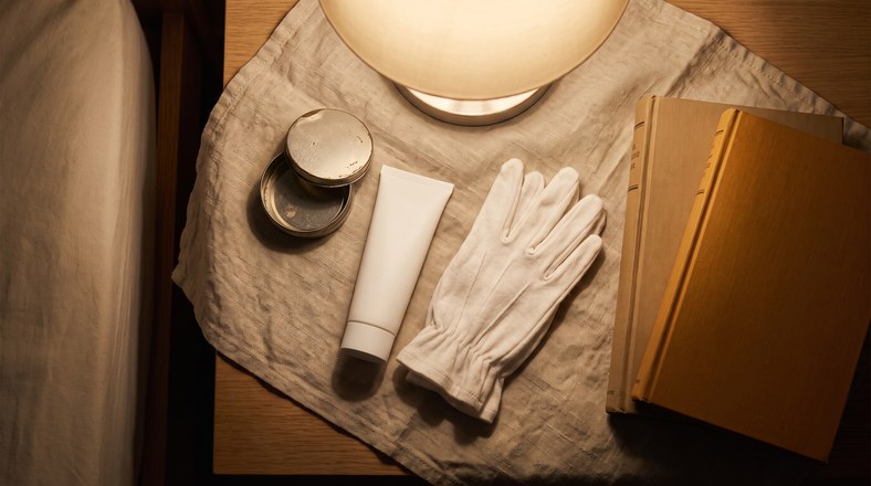 Lip balm, hand cream and cotton gloves on a bedside table for overnight repair of dry skin from central heating